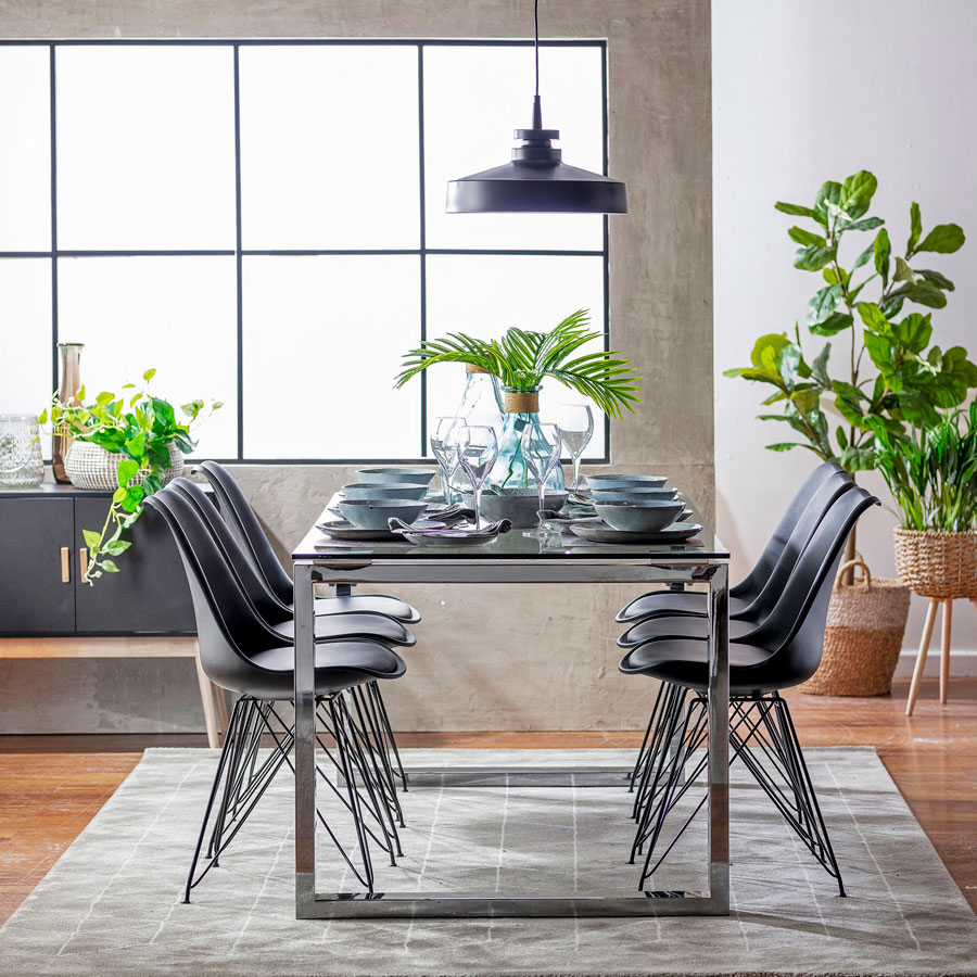 Comedor con una mesa rectangular y seis sillas. Está sobre una alfombra gris. Hay un arrimo negro al fondo, decorado con jarrones.