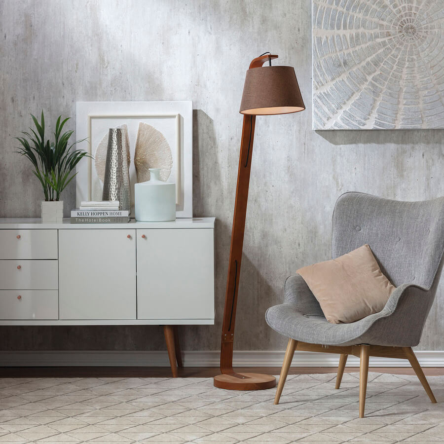 Poltrona gris combinada con una lámpara de pie de madera con pantalla café y un mueble blanco con patas de madera.
