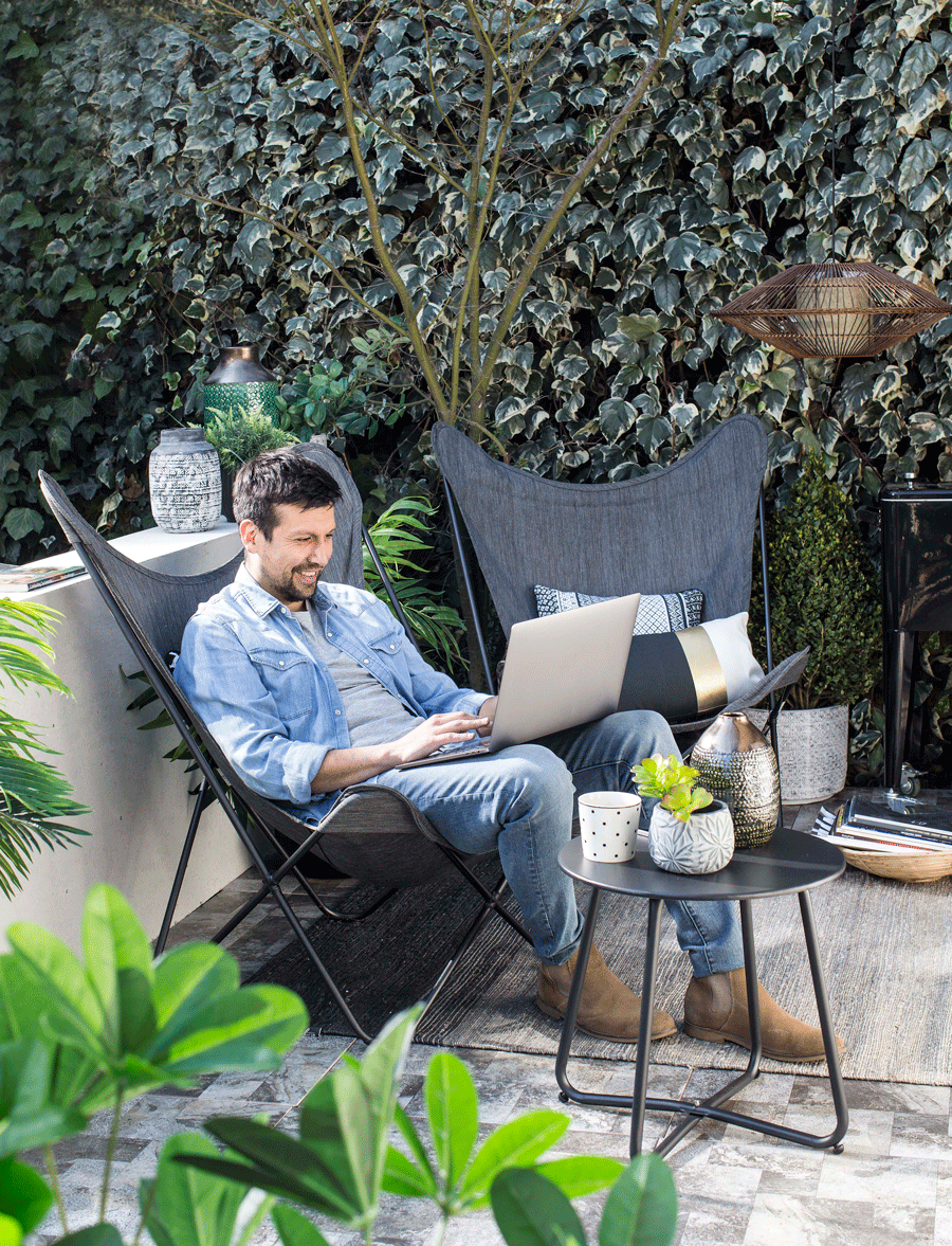 Hombre sentado en silla en la terraza comunicandose por la computadora