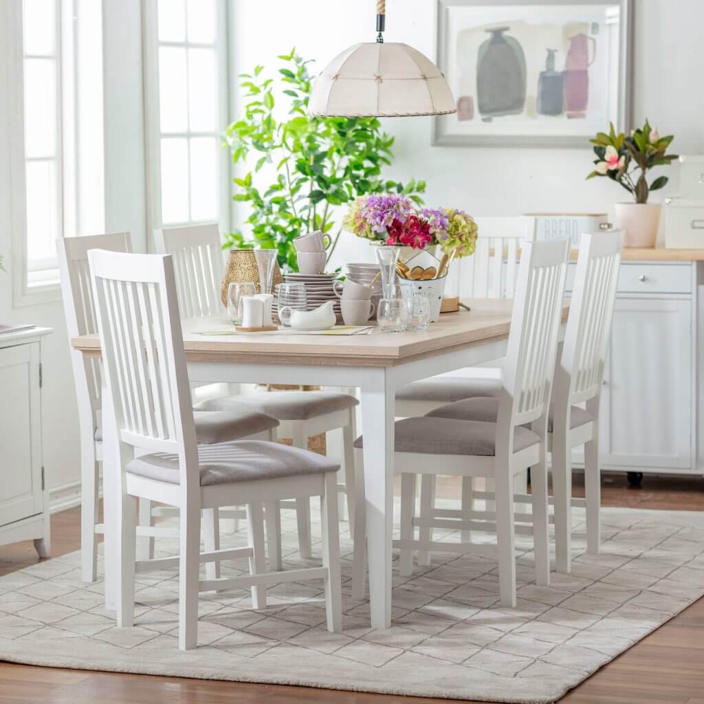 Comedor con una alfombra blanca que contiene una mesa de madera blanca y seis sillas blancas.