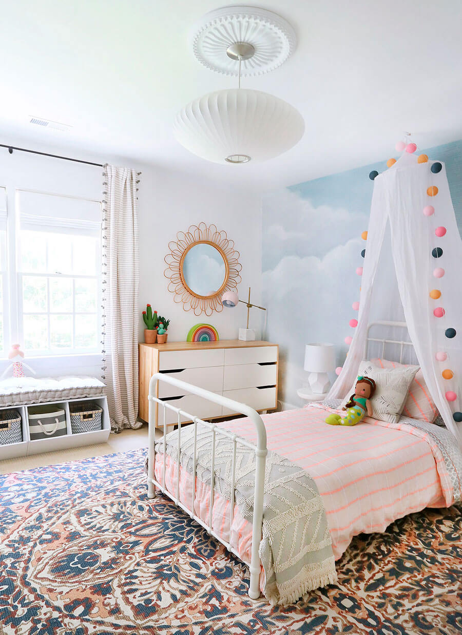 Un dormitorio grande infantil con una alfombra con ilustraciones que contiene una cama de metal con una dosel. 