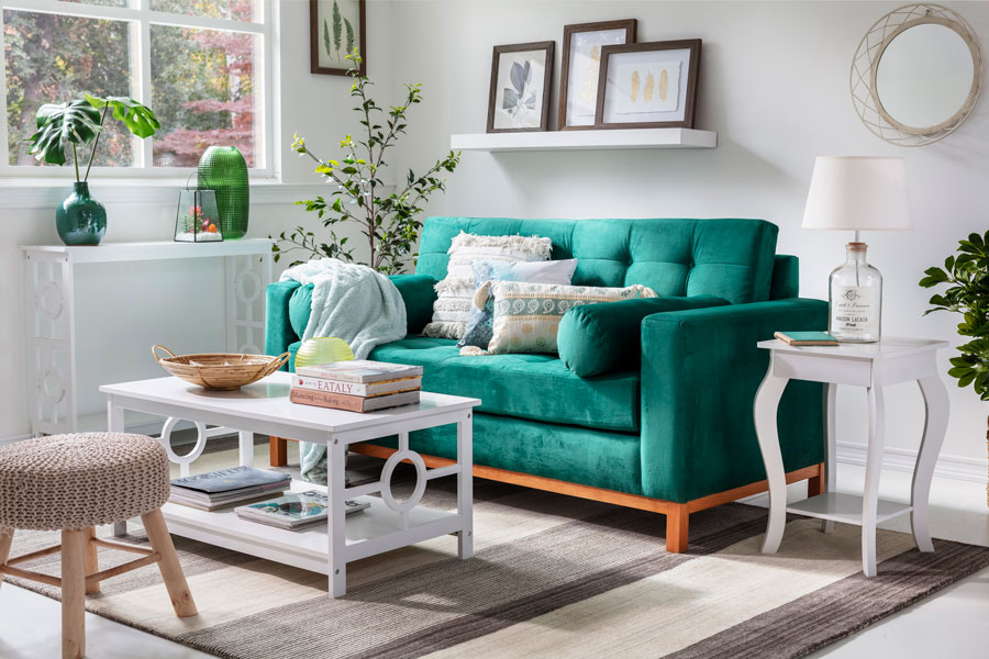 Living con un sofá verde esmeralda y una mesa de centro, mesa lateral y arrimo blancos. Sobre los muebles hay jarrones, lámparas y decoraciones.