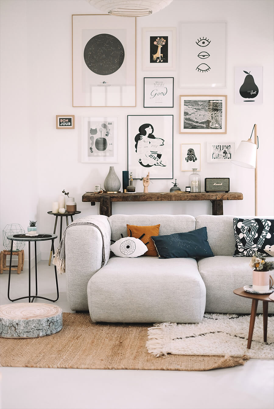 Living con un sofá blanco. Detrás de ella hay una pared blanca con un arrimo de madera y sobre ella una combinación de cuadros con ilustraciones.