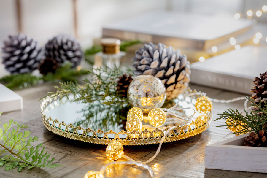 Centro de mesa con decoraciones navideñas, como una bandeja dorada con pinos y eucaliptus.