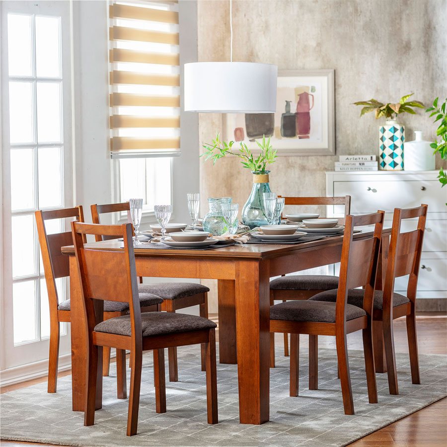 Mesa de comedor de madera rectangular con seis sillas del mismo material. Están sobre una alfombra gris y, sobre la mesa, están distribuidos platos, copas y jarrones.