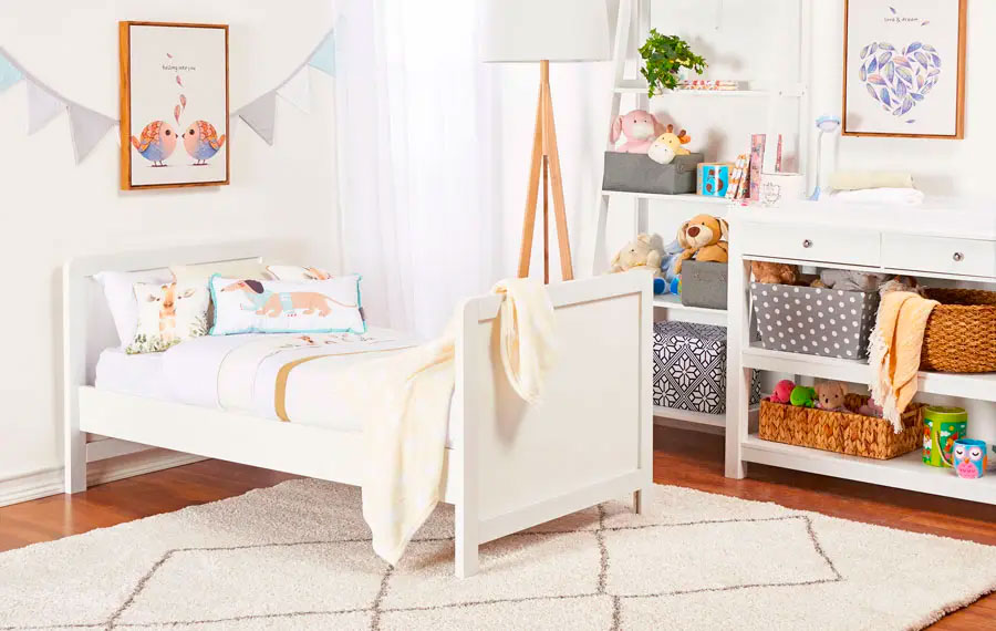 Habitación infantil con una cama, arrimo y estante estilo escalera blancos y una cortina de tela blanca.