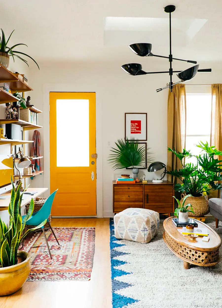 Espacio del hogar con techo y paredes blancos con suelo de madera cubierto con varias alfombras. Hay una puerta amarilla con ventana.