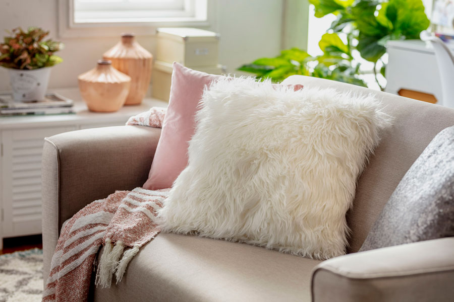Sofá de cuero de color rosado con un cojín decorativo peludo blanco