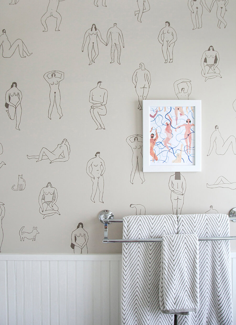 Papel mural para baño con ilustraciones simples de personas desnudas y un marco con ilustraciones de personas desnudas sobre un toallero de metal con toallas grises.