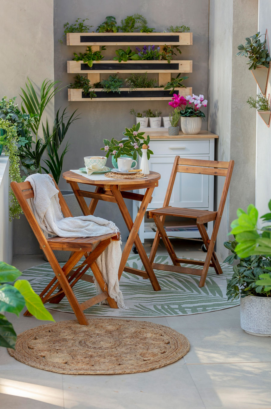 Un espacio al aire libre con muebles de terraza de madera: una mesa y 2 sillas. Es una idea para hacer un home office exterior.