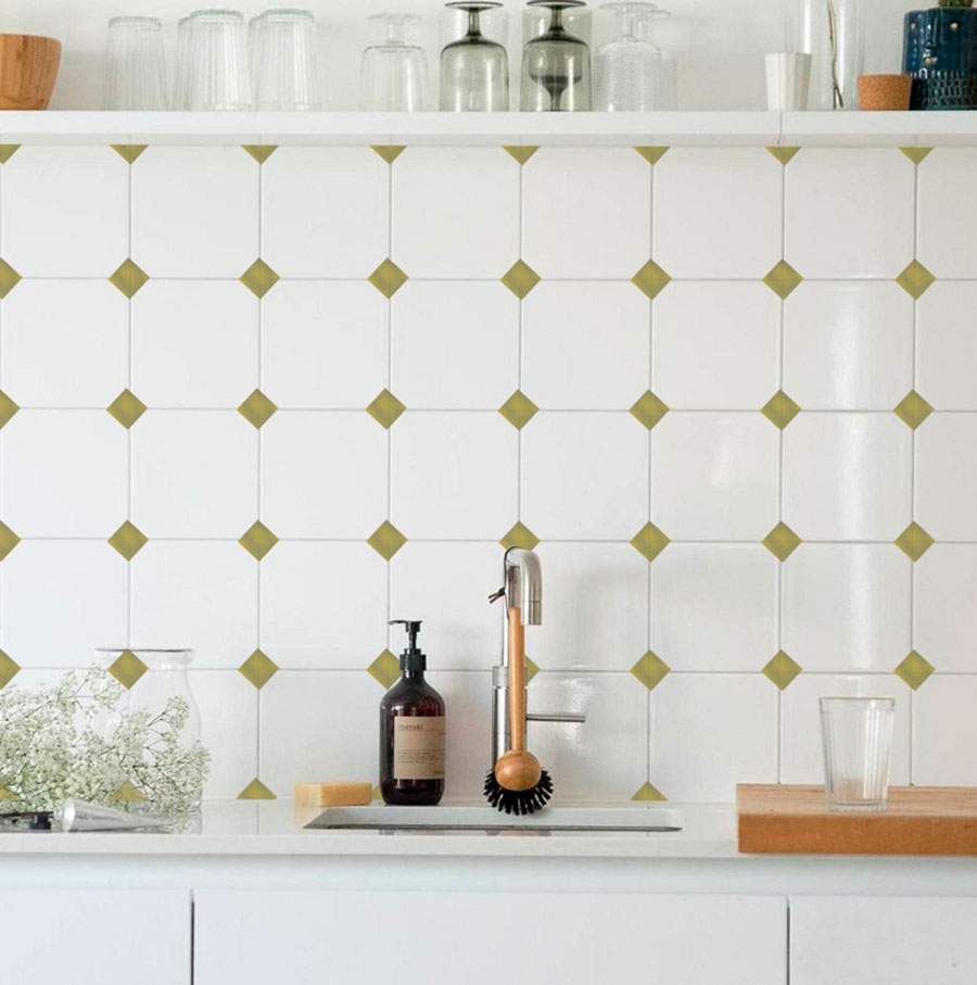Detalle de la cocina con un salpicadero de mosaicos blancos y verde oliva. La cubierta, estantes y muebles de cocina son blancas.