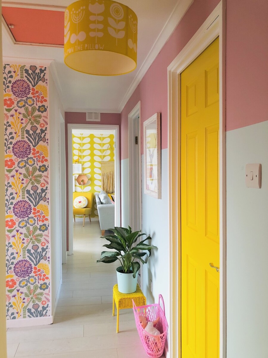 Pasillo de un hogar con paredes pintadas de blanco y rosado, puertas rosadas y, otra parte de la pared cubierta de papel mural con patrones florales.