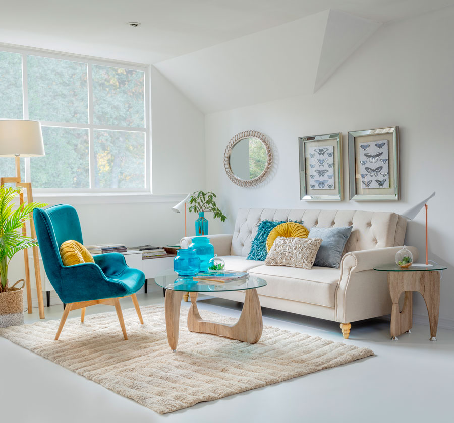 Un living con sofá color crema, una poltrona gris, arrimo, mesa de centro y lateral de vidrio con base de madera.