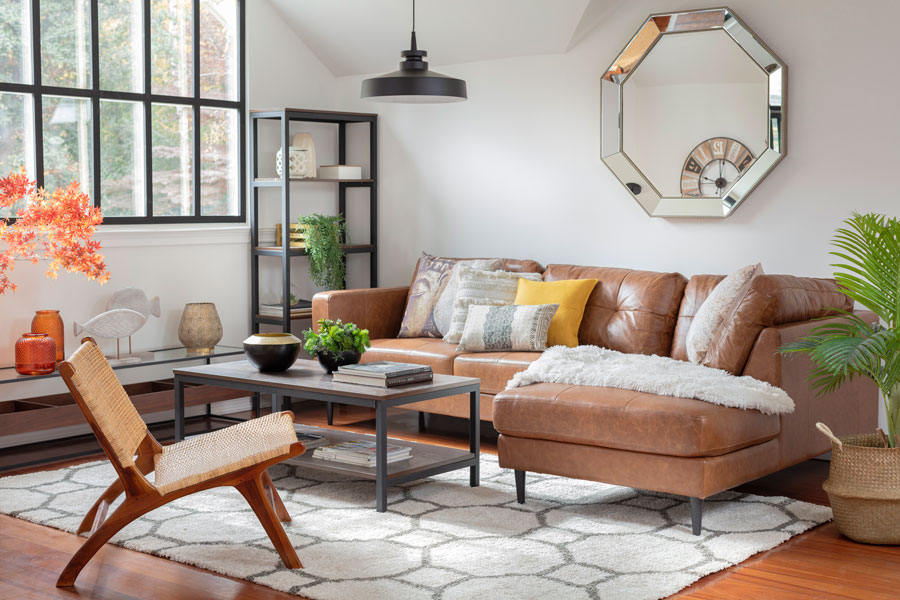 Una sala de estar de tonos claros destaca con elementos de decoración con un sofá modular de cuero, una mesa de centro de tonos grises y un espejo plateado.
