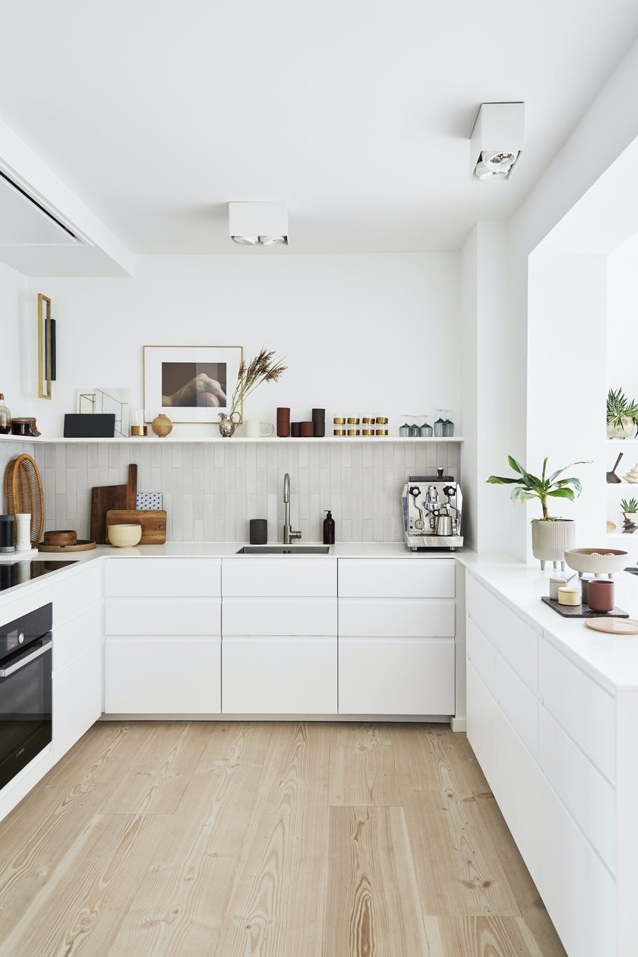 Una cocina con paredes y muebles blancos se complementa con electrodomésticos y decoraciones en tonos madera y métalicos.