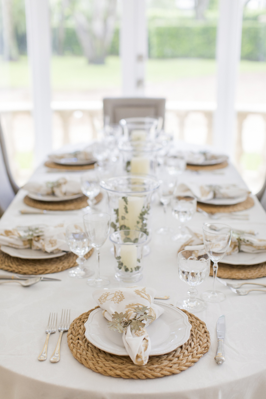 Una mesa muy elegante con copas de vidrio y platos blancos, sobre individuales de fibras naturales.