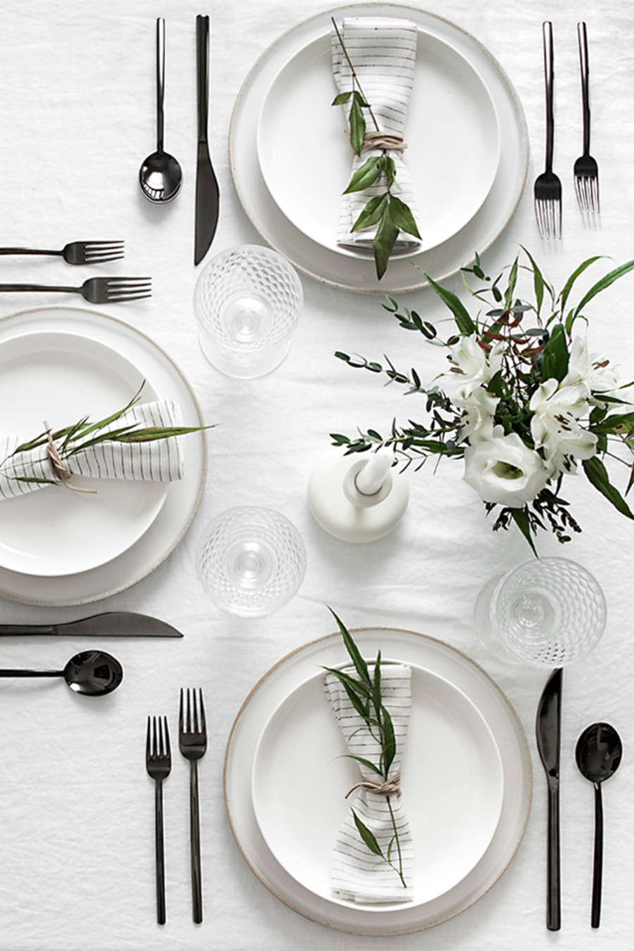 Una mesa de comedor con mantel de lino blanco y platos del mismo color reflejan la decoración de una mesa con elementos blancos. 