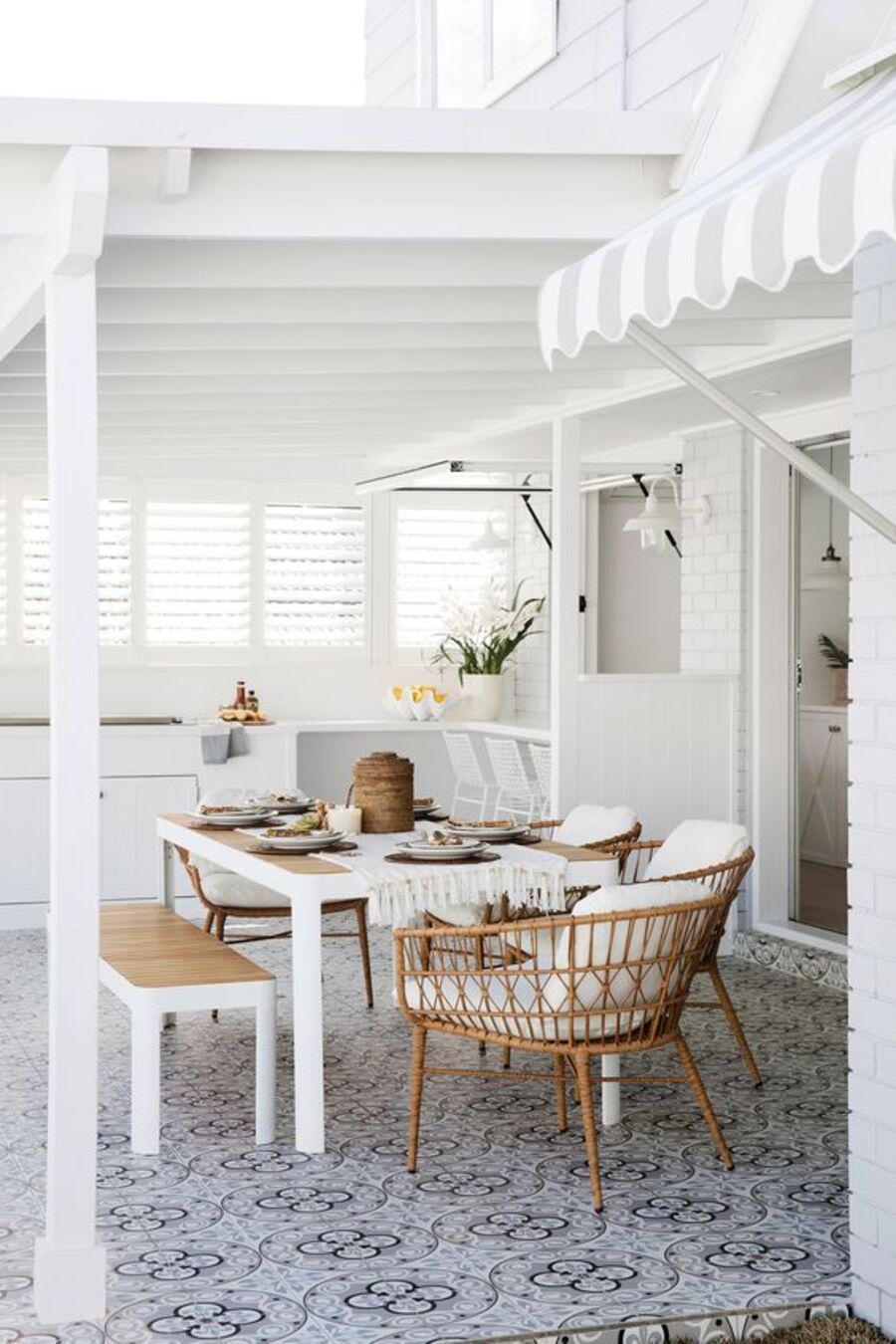 Un comedor de terraza con tonos de madera y muebles de fibras naturales resaltan en un espacio de paredes blancas. 