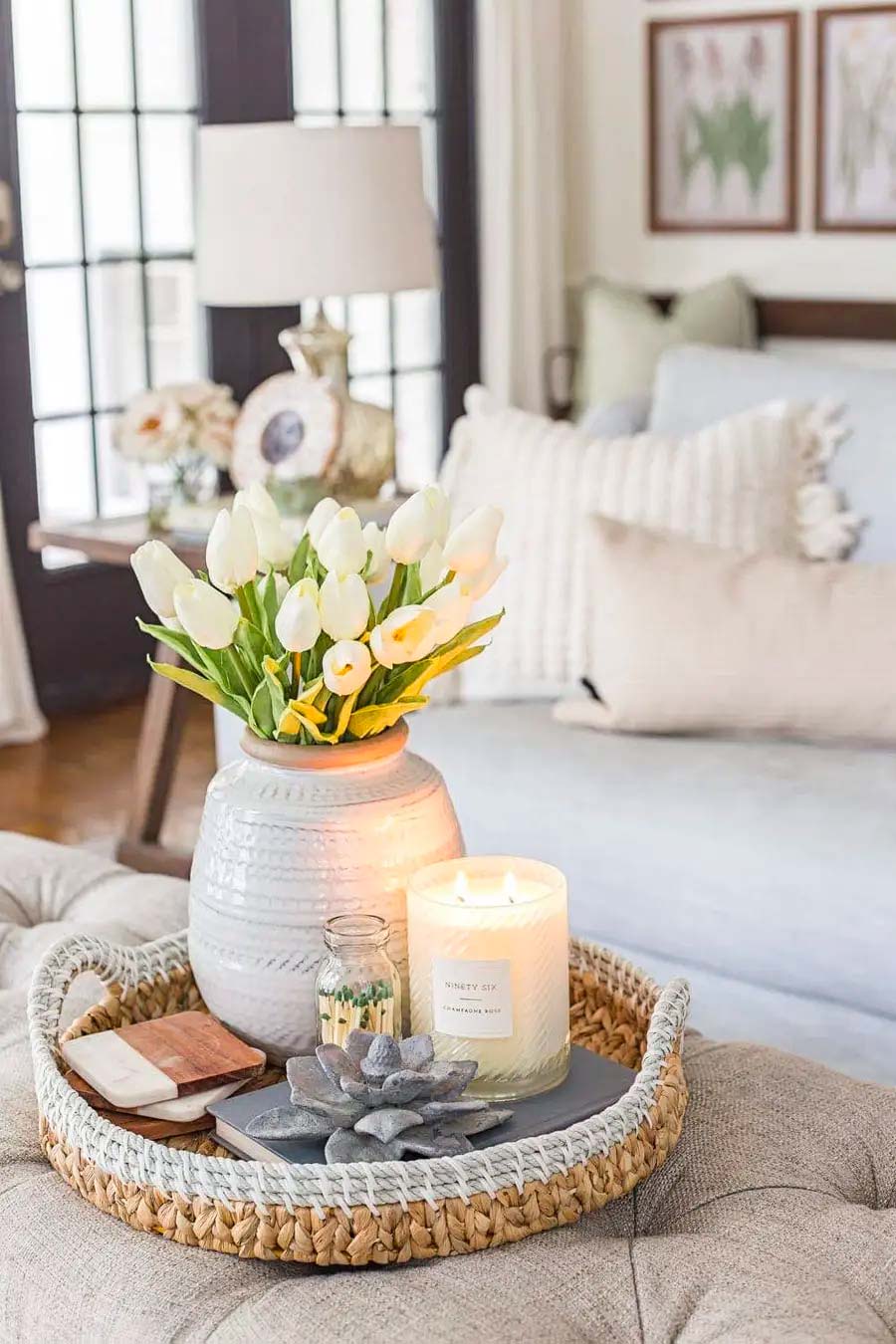 Detalle de living de una bandeja de mimbre con un florero blanco con flores blancas, una vela blanca prendida y otras decoraciones.