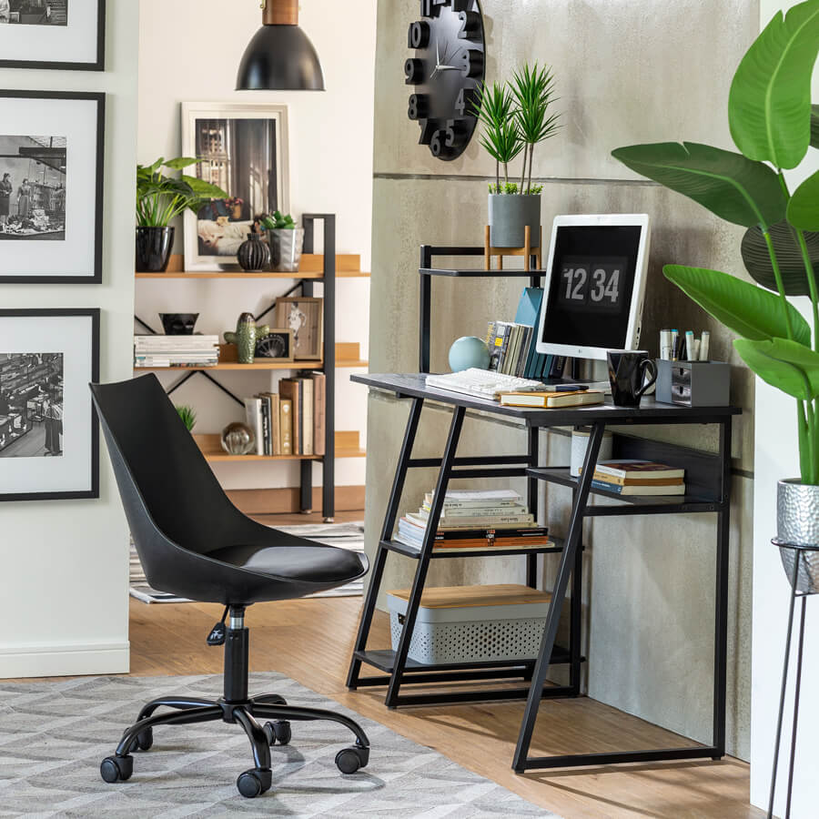 Espacio de trabajo estilo ejecutivo urbano con un escritorio negro sin cajones combinado con una silla de oficina negra con apoyabrazos sobre una alfombra gris. Al fondo hay un mueble de madera con detalles negros. Sobre el escritorio hay una lámpara colgante negra y un reloj redondo negro.