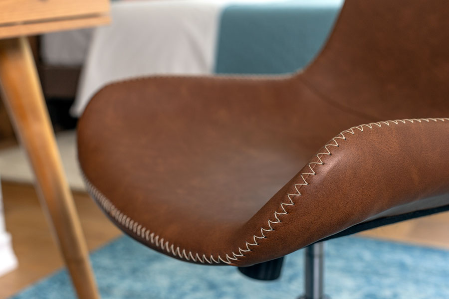 Detalle de una silla de escritorio, de un material similar al cuero y costuras blanco crudo.