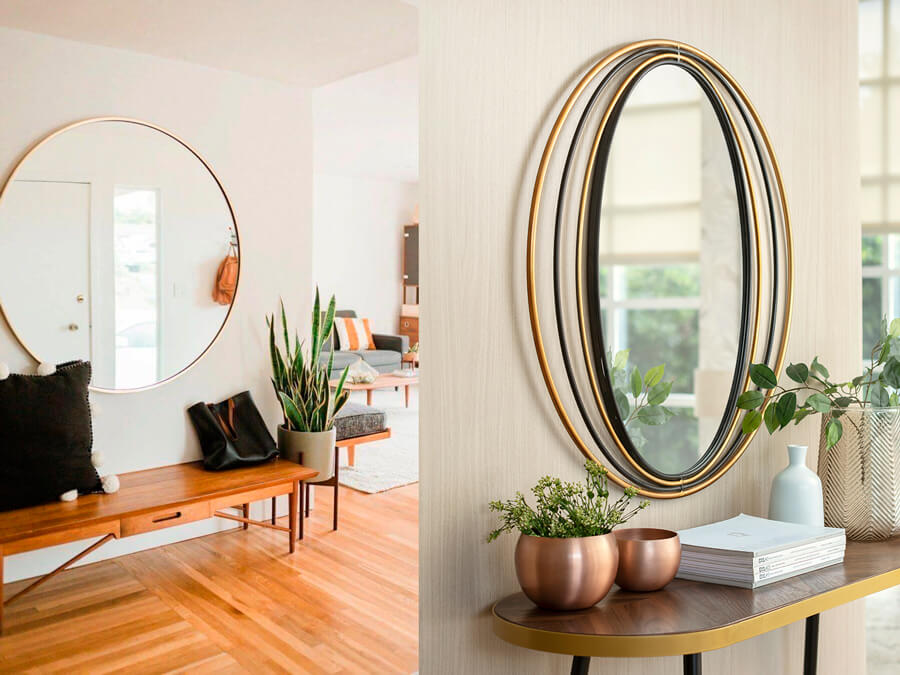 Dos recibidores, uno con un espejo decorativo redondo y el siguiente con un espejo ovalado. Los dos tienen marcos dorados y están sobre una repisa de madera.