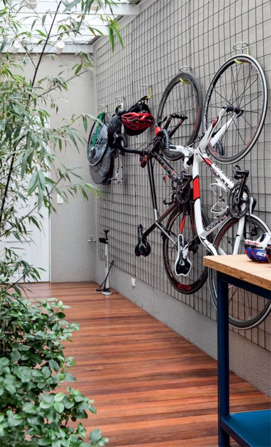 Rejilla de metal pegada a una pared gris, desde la cual cuelgan dos bicicletas, sus respectivos cascos y otros elementos deportivos. 