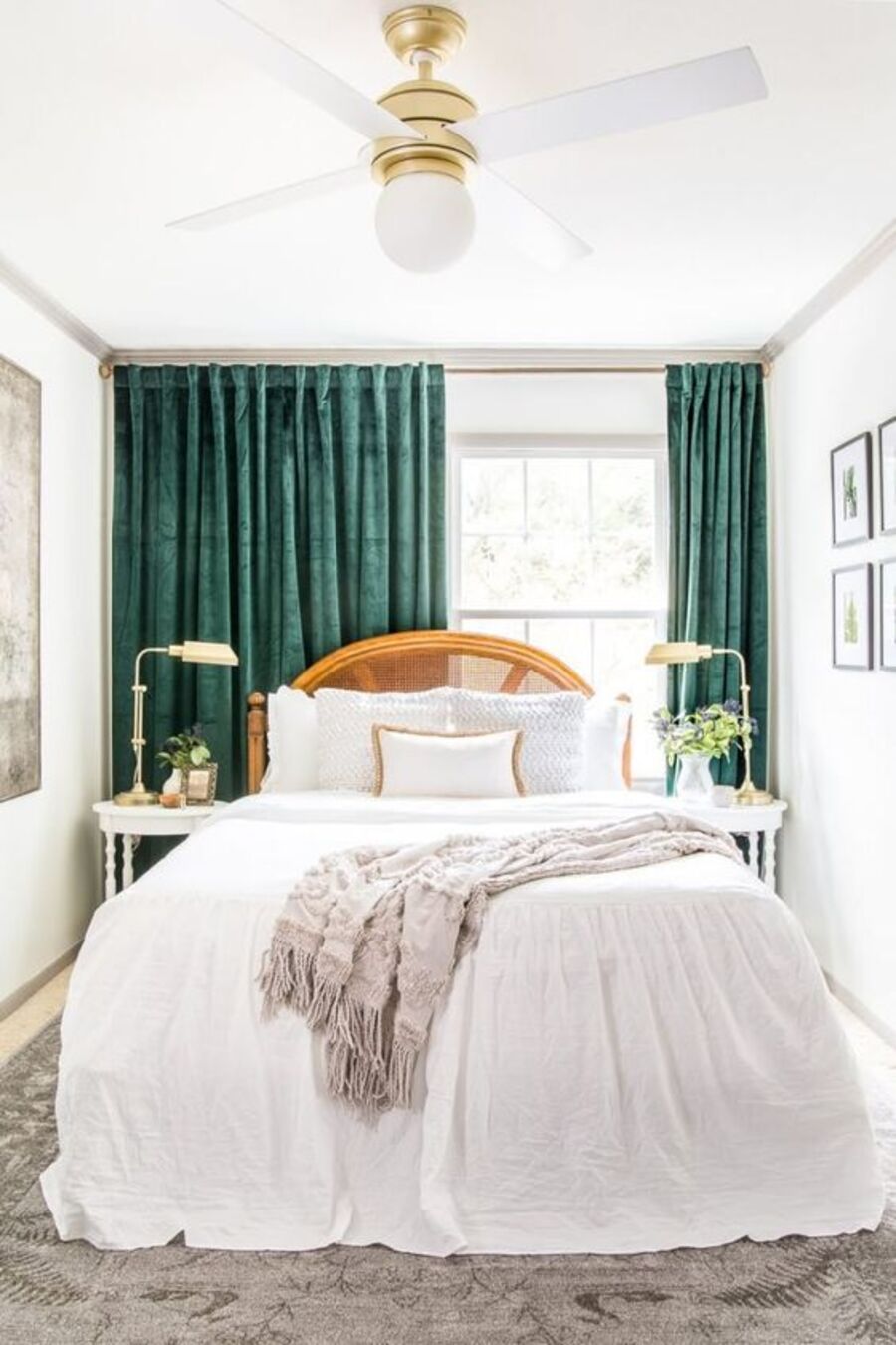 Dormitorio de paredes, techo, veladores y ropa de cama blancos. Las cortinas son de terciopelo verde oscuro, la alfombra y manta sobre la cama son grises y la cama, de madera. Sobre el techo cuelga una lámpara y ventilador blanco con soporte dorado. 