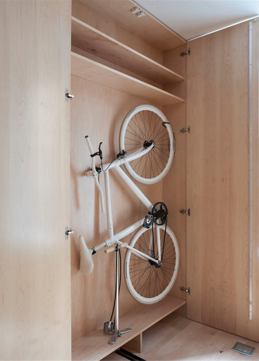 Clóset de madera clara abierto, en cuyo interior cuelga una bicicleta blanca.
