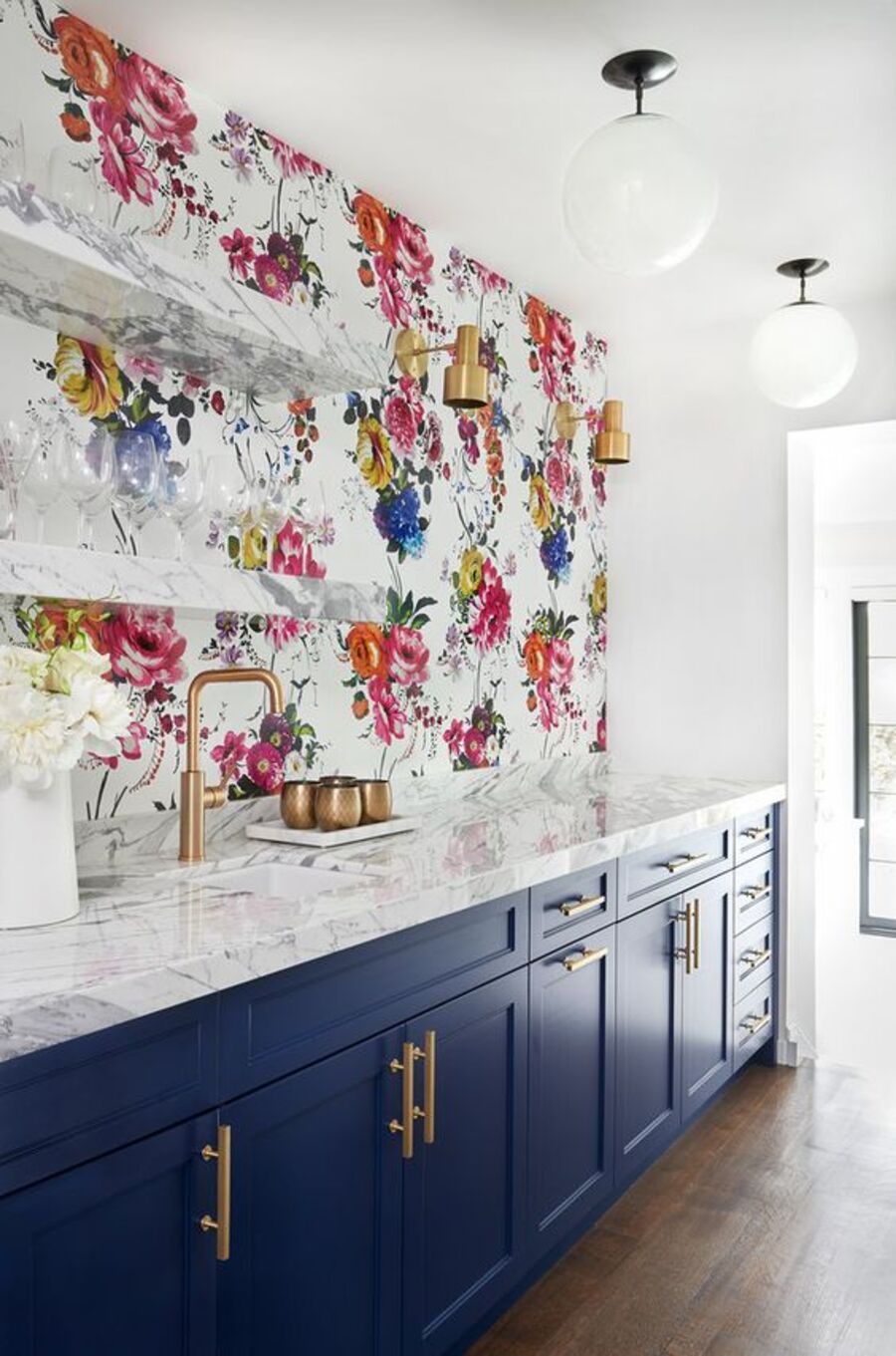 Cocina con papel mural de flores rosadas, rojas, amarillas y azules, mueble de cocina azul con cubierta de mármol y repisas de mármol.