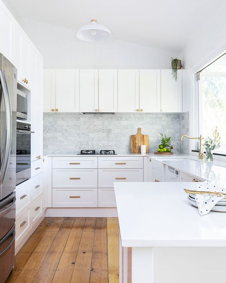 Cocina en forma de U con muebles blancos y cubierta blanca. El piso es de madera, el techo blanco y la pared tiene un adhesivo vinílico gris.