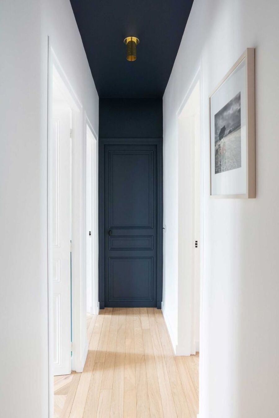 Largo pasillo de muros blancos y piso de madera clara. Tanto el techo como la puerta y muro del fondo está pintados en azul marino.