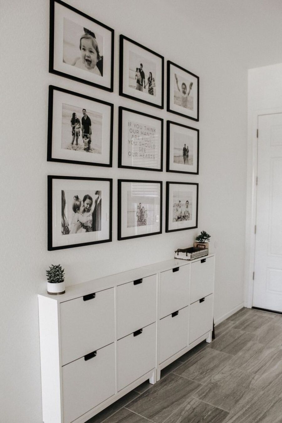 Pasillo de paredes blancas decorado con 9 fotografías en blanco y negro, enmarcadas en marcos negros. Debajo hay un mueble zapatero blanco.