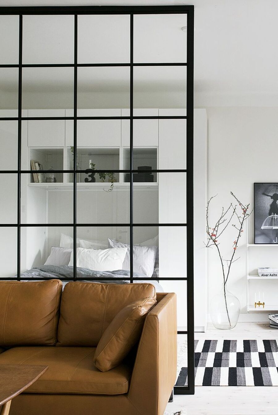 Dormitorio separado de un living o sala de estar por un separador de vidrio con cuadrados de marco negro. 