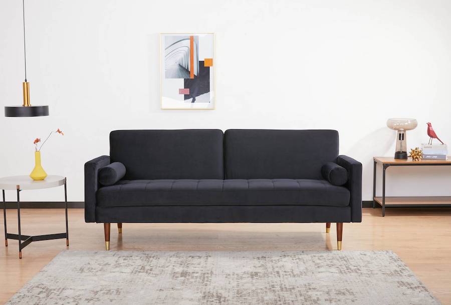 Futón negro elegante en una sala de estar. Junto a él hay una mesa lateral redonda y al frente, una alfombra en tonos neutros.