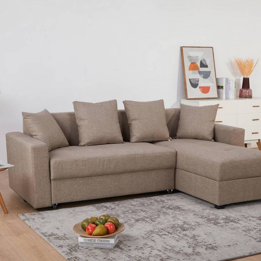 Living con un sofá seccional color café claro. Sobre él hay cuatro cojines del mismo color del sofá. 