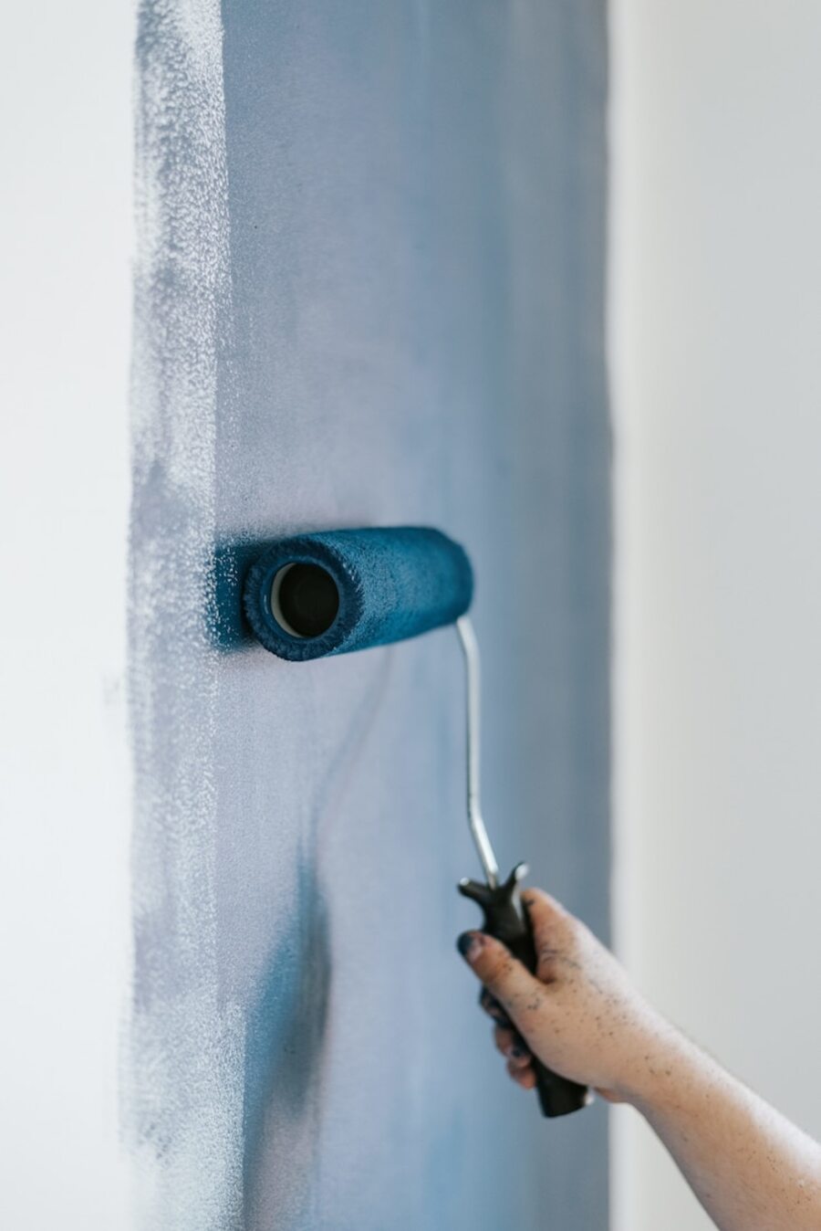Detalle de una pared que está siendo pintada de azul marino con un rodillo sostenido por una mano.