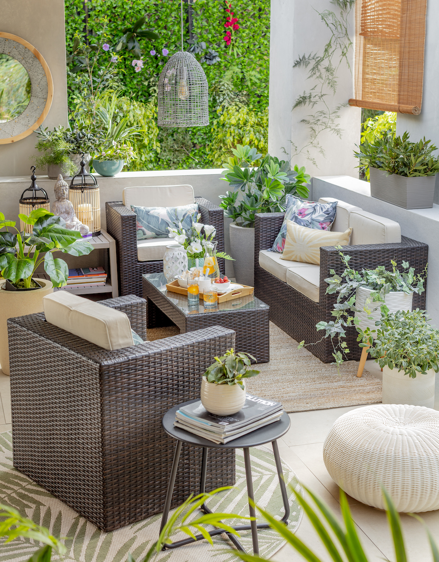 Living de terraza de ratán con cojines blancos y diferentes plantas en maceteros alrededor de los muebles
