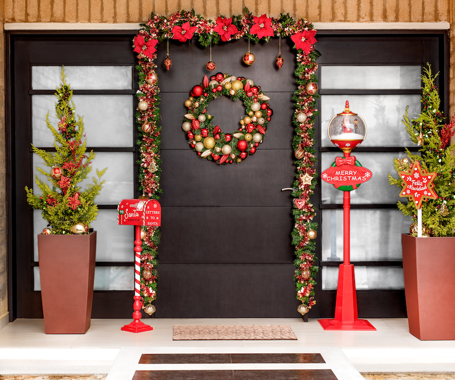 Entrada de una casa con una gran puerta decorada con guirnaldas y adornos navideños de colores rojos, dorados y verdes.