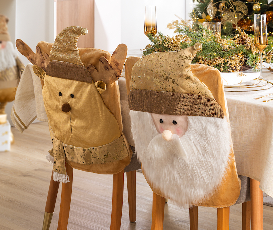Detalle de una mesa de comedor, cuyas dos sillas están decoradas con respaldos navideños, una de un reno y la otra de viejito pascuero. Ambos en tonos dorados.