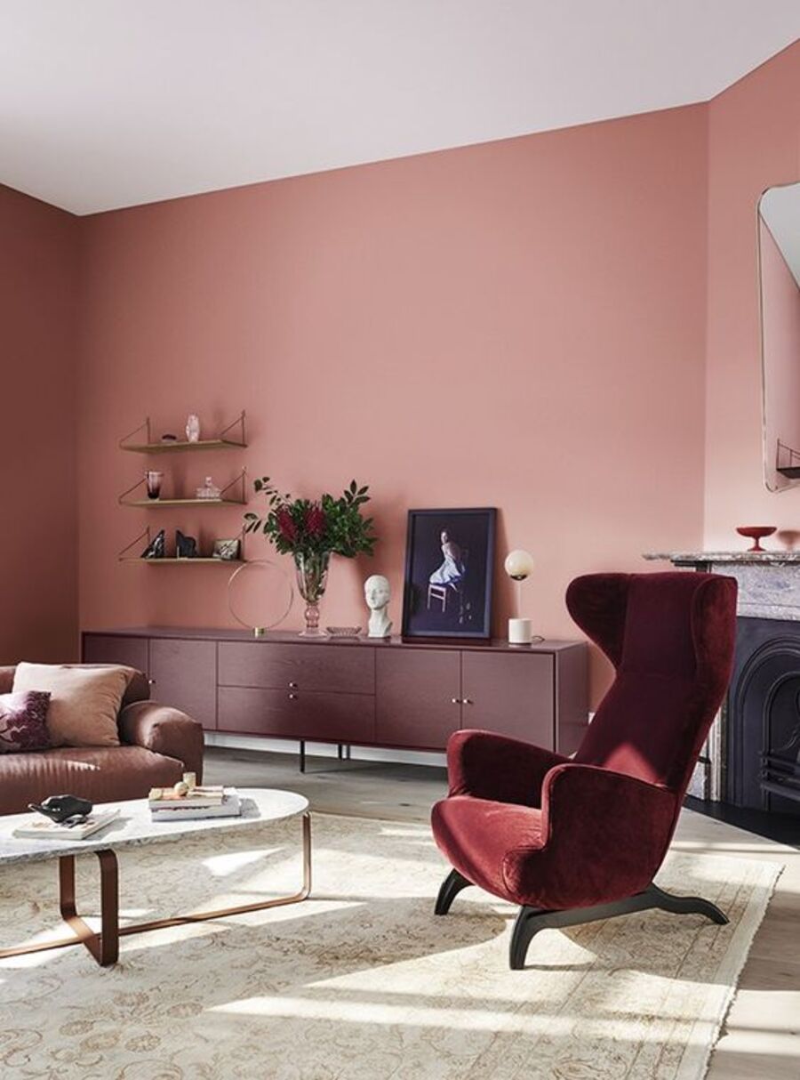 Sala de estar con paredes rosadas, sillón color magenta, buffet burdeos, sofá café y mesa de centro de mármol. Sobre el buffet hay distintos adornos, un cuadro y un florero con flores magenta.
