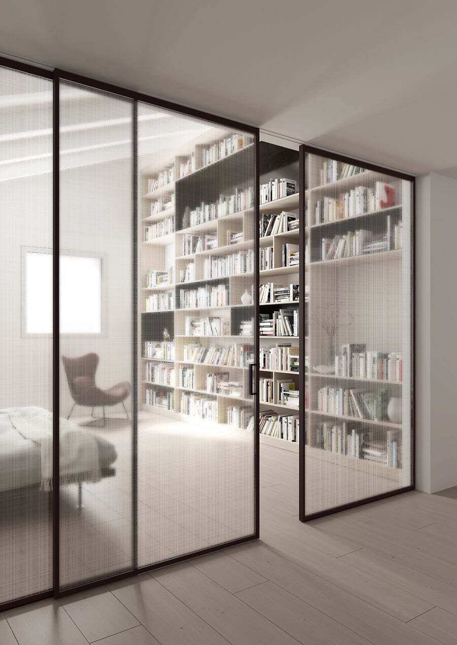 Dormitorio con una gran biblioteca empotrada llena de libros. Hay un gran ventanal de vidrio con puerta corredera, también de vidrio, que separa el dormitorio del pasillo. 