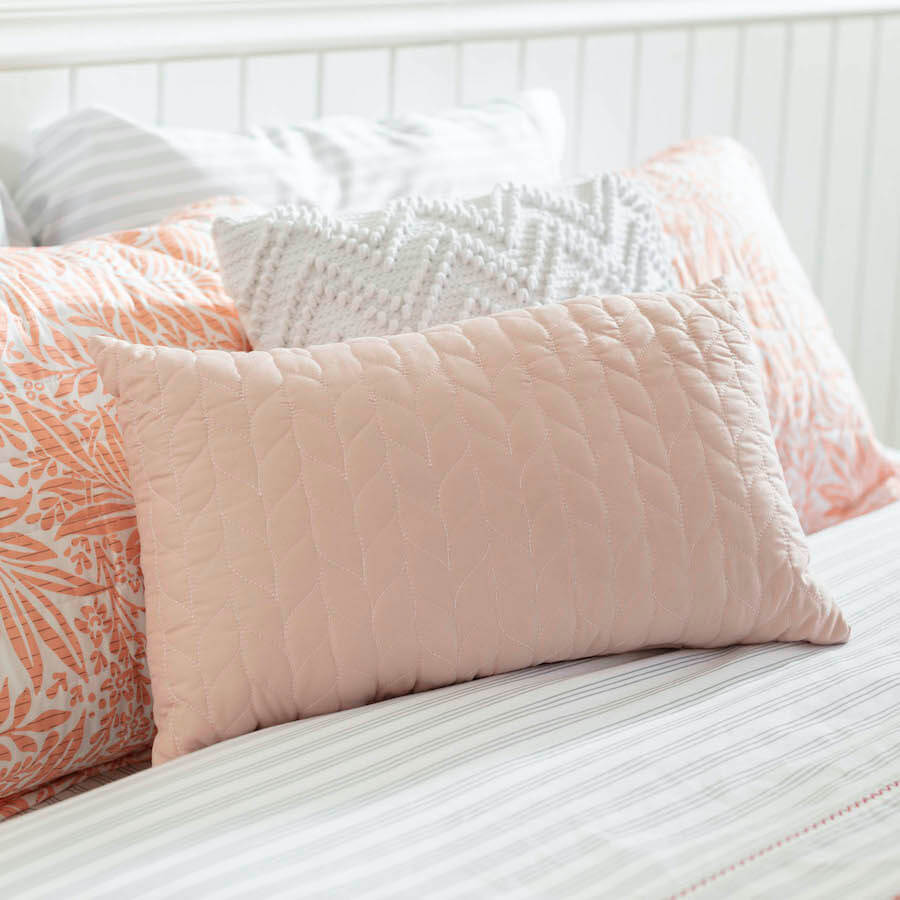 Cojines de tonalidades blancas, grises y rosadas en una cama con sábanas grises.