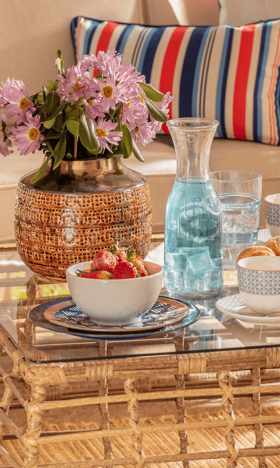 Mesa de centro con un jarrón marrón con flores, jarra de agua y otros menajes de mesa.