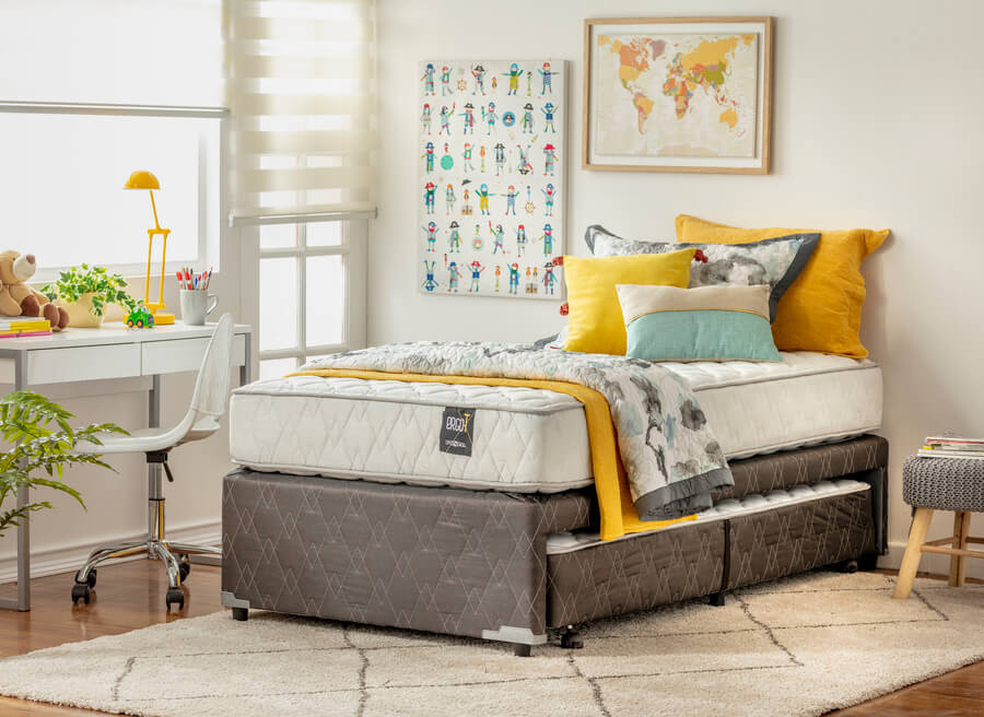 Dormitorio infantil moderno. Cama nido de una plaza, con colchón expuesto, ropa de cama en tonos blanco, gris y amarillo. Muros blancos y alfombra blanca con líneas grises.