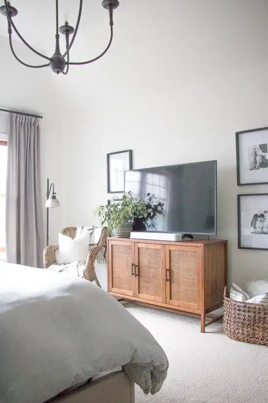 Dormitorio de estilo clásico. Muros blancos, alfombra blanca. Mueble de televisión de madera clara y puertas de fibras naturales. Muro galería simétrico, al costado del televisor, con cuadros en blanco y negro.