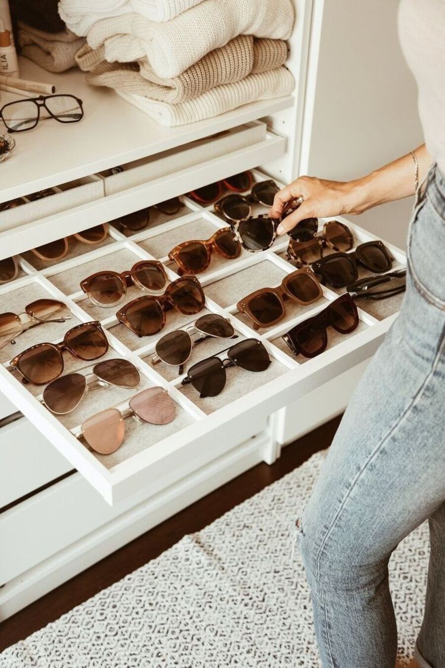 Cajón de closet con organizador de cajones para gafas o lentes de sol. Cajón bajo con separaciones. Sweaters en tonos blanco y beige.