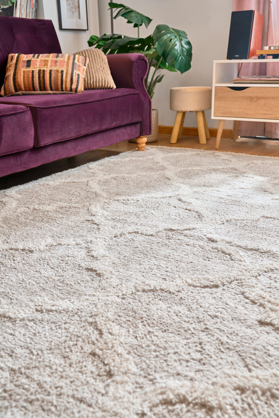 Living pequeño con medidas de alfombras ideales. El sofá velvet color morado tiene solo las patas delanteras sobre la alfombra shaggy gris.