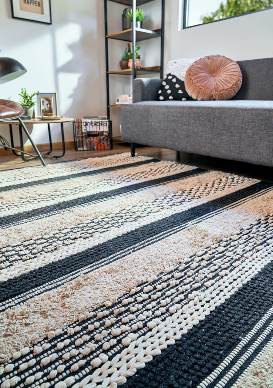 Living con un futón gris con solo las patas delanteras sobre una alfombra con tejidos trenzados blancos y negros. 