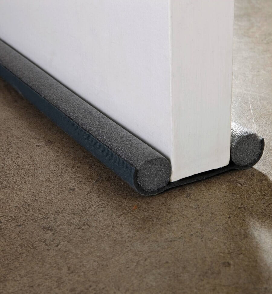 Detalle de burlete para puerta doble, de plumavit color negro, útiles para ahorrar energía al mantener el calor al interior. Puerta blanca y alfombra café.